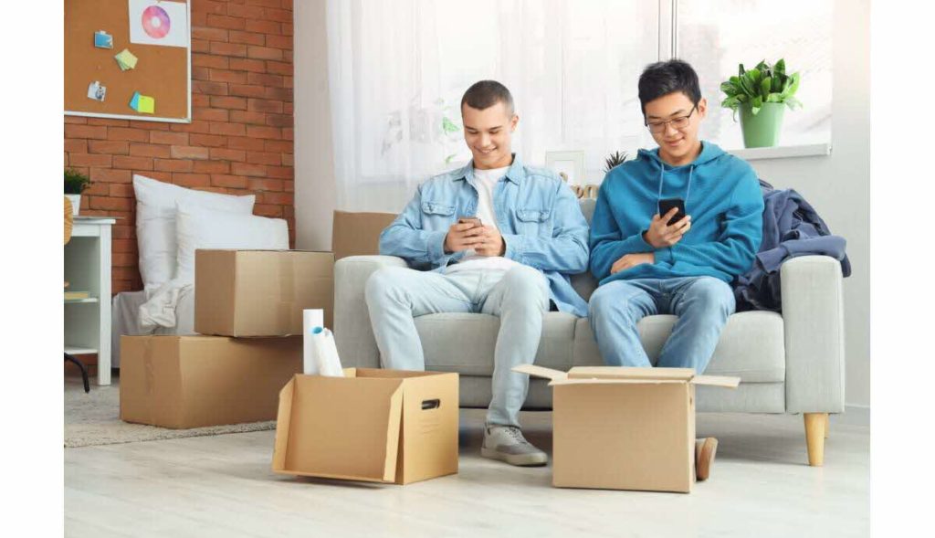 Deux étudiants assis dans un fauteuils avec leur téléphone à la main et un carton à leurs pieds